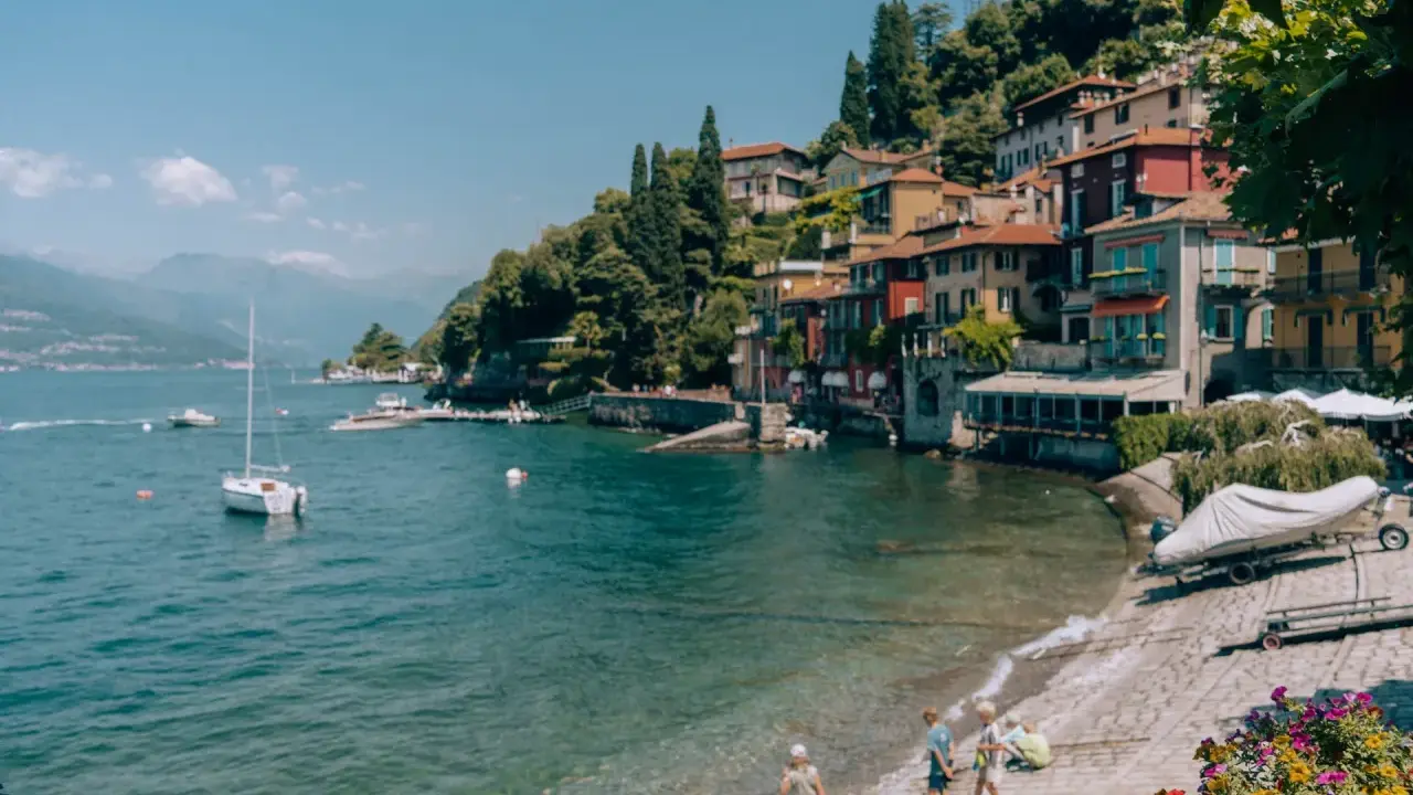 Urokliwe como miasto nad jeziorem, z kolorowymi domami na wzgórzu, łodziami na wodzie i dziećmi bawiącymi się na plaży.