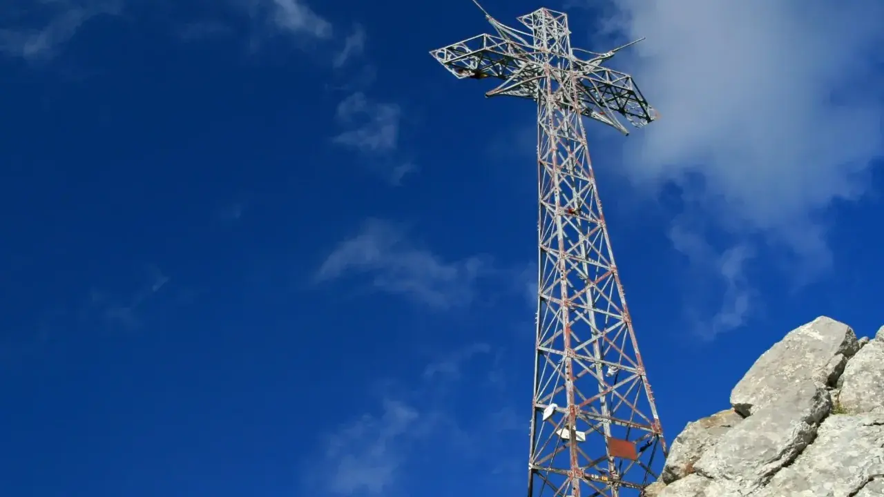 Metalowy krzyż na skalistym szczycie Giewontu pod błękitnym niebem z chmurami.