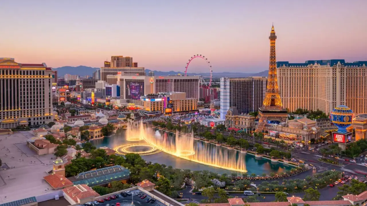 Las Vegas, miasto hazardu w USA, nocą. Widać fontanny, wieżę Eiffla i diabelski młyn.