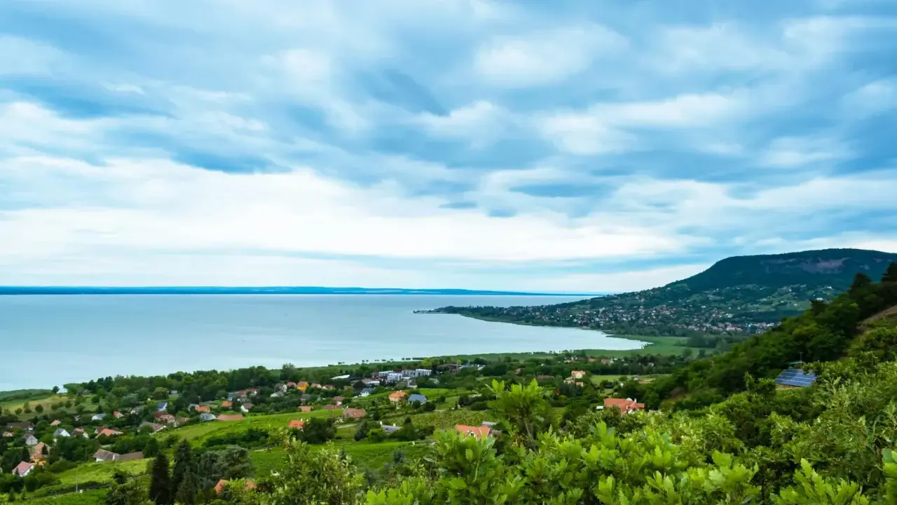 Widok na Balaton z góry, z zielonymi wzgórzami i domkami. W oddali widać jezioro i plażę.