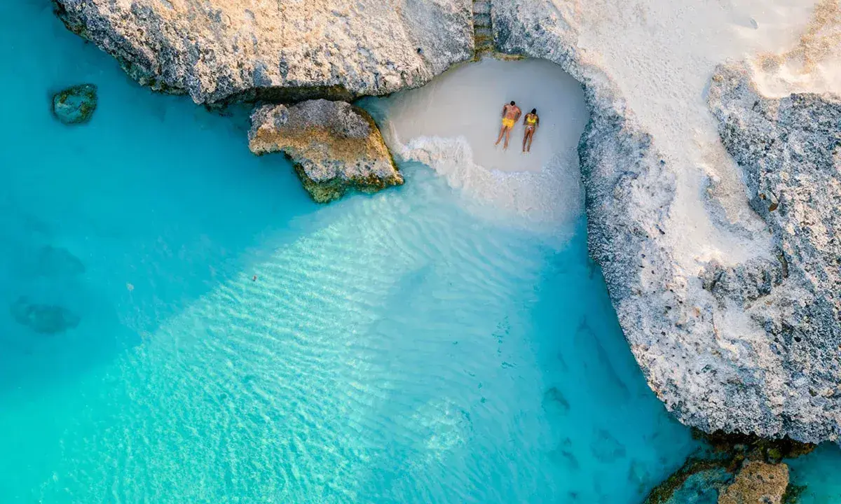 Para relaksuje się na ukrytej plaży na wyspie Aruba, otoczonej turkusową wodą i skalistymi klifami.