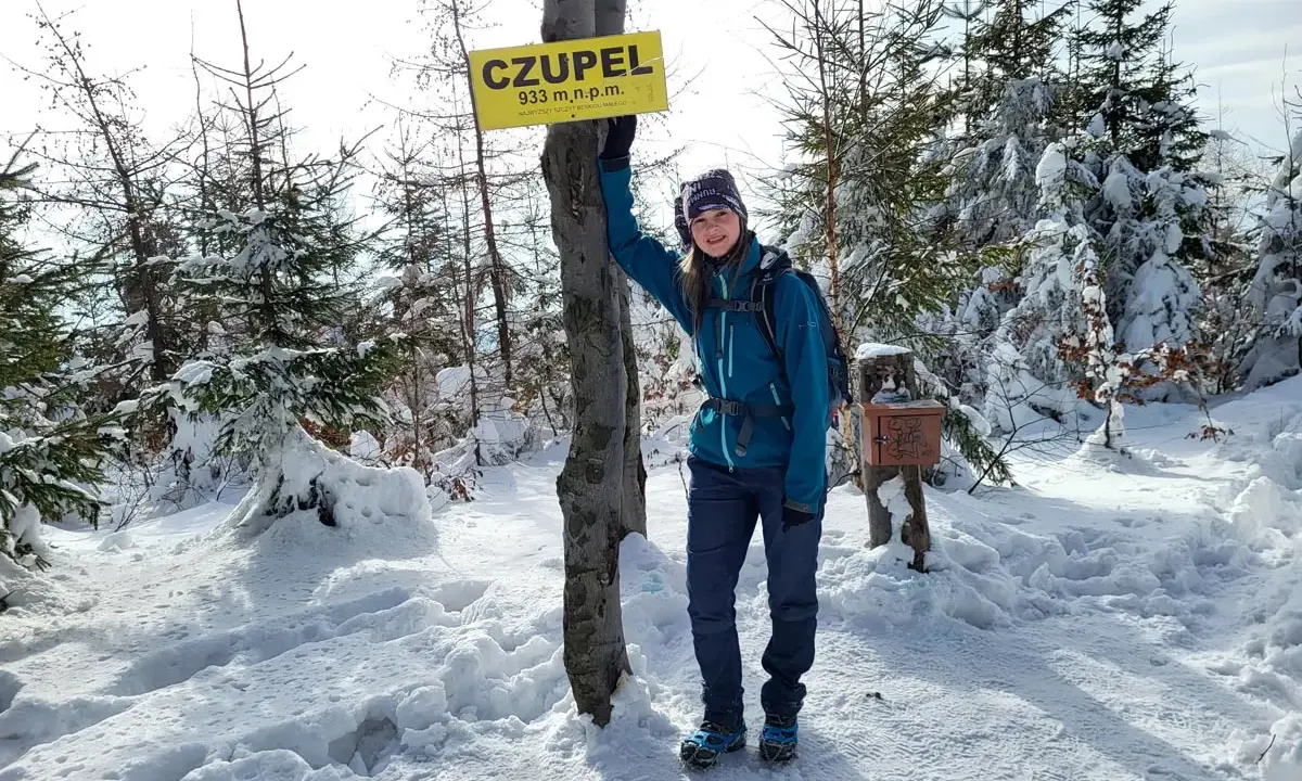 Dziewczyna na szczycie **Czupel** (933 m n.p.m.) w zimowej scenerii, z tabliczką i skrzynką na pieczątkę.