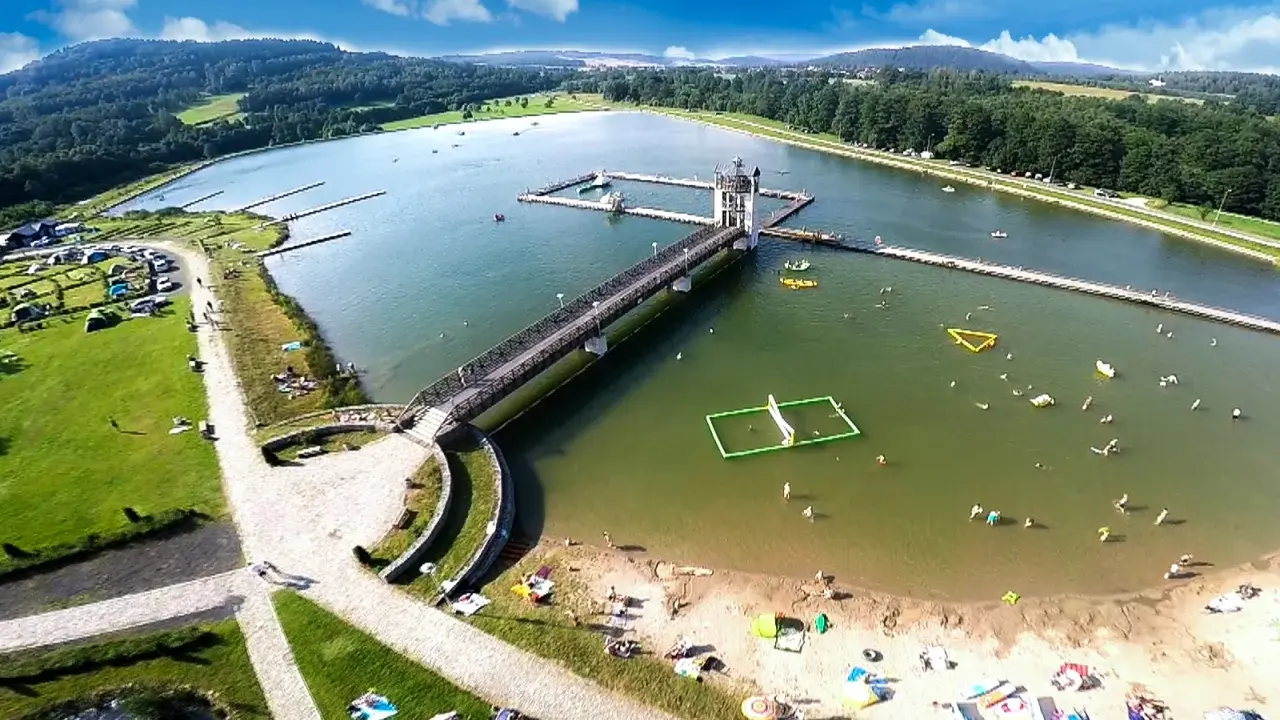 Letnia rekreacja nad zalewem, gdzie czarna góra stanowi malownicze tło dla wodnych atrakcji i wypoczynku na plaży.