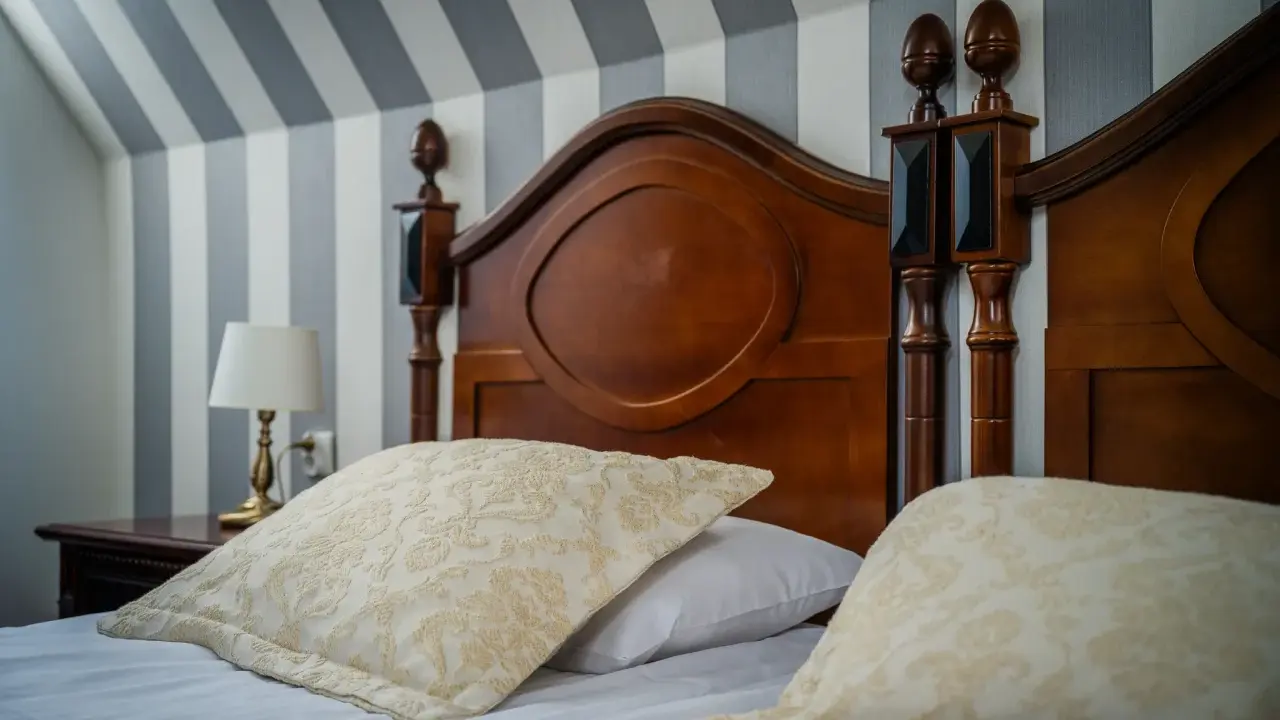 Eleganckie łóżko z drewnianym zagłówkiem i ozdobnymi poduszkami. Ciekawe, ile wynosi ryczałt za nocleg w takim miejscu?