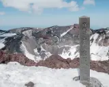 Kamienna tablica z japońskimi znakami na szczycie świętej góry na Honsiu. W tle widać krater wulkanu z resztkami śniegu.