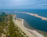 Piaszczysta wyspa na Bałtyku, otoczona wodą i zielenią, tworzy malowniczy krajobraz.