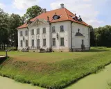 Pałac w Choroszczy otoczony fosą i zielenią, z drewnianym mostkiem prowadzącym do wejścia.