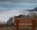 Drewniana ławka na tle morza chmur i gór. Widok z **Abchazji** zapiera dech w piersiach, idealne miejsce na chwilę zadumy.