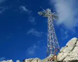 Metalowy krzyż na skalistym szczycie Giewontu pod błękitnym niebem z chmurami.