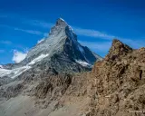Majestatyczne szwajcaria góry z ośnieżonym szczytem Matterhorn w tle i skalistym zboczem na pierwszym planie.