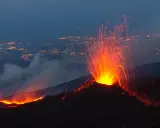 Spektakularna erupcja Etny nocą, z płynącą lawą i deszczem iskier nad oświetlonym miastem.