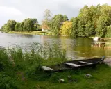 Łódka na brzegu, w tle zielone drzewa i domki nad wodą. Widok na największe jezioro w Polsce.