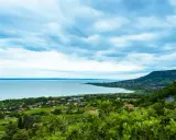 Widok na Balaton z góry, z zielonymi wzgórzami i domkami. W oddali widać jezioro i plażę.
