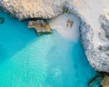 Para relaksuje się na ukrytej plaży na wyspie Aruba, otoczonej turkusową wodą i skalistymi klifami.