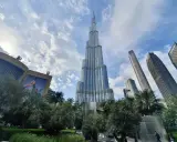 Burj Khalifa, najwyższy budynek w Dubaju, wznosi się dumnie na tle błękitnego nieba z chmurami. Otoczony zielenią i innymi drapaczami chmur.