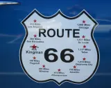 Tablica z napisem "ROUTE 66" i odległościami do miast, np. Chicago, Los Angeles, St. Louis.