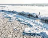 Ludzie spacerują po zamarzniętej plaży z lodowymi formacjami przypominającymi góry.