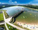 Letnia rekreacja nad zalewem, gdzie czarna góra stanowi malownicze tło dla wodnych atrakcji i wypoczynku na plaży.