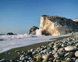 Kamienista plaża na wyspie Afrodyty, gdzie fale rozbijają się o skaliste klify.