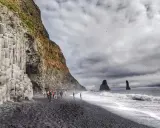 Skały bazaltowe na plaży Reynisfjara, czarny piasek, fale i skalne iglice w morzu.