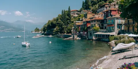 Urokliwe como miasto nad jeziorem, z kolorowymi domami na wzgórzu, łodziami na wodzie i dziećmi bawiącymi się na plaży.