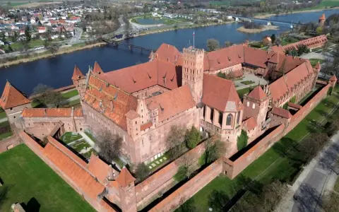 Malbork, największy zamek w Europie, rozciąga się wzdłuż rzeki, otoczony murami obronnymi i zielonymi dziedzińcami.