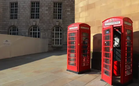 Klasyczne czerwone budki telefoniczne na brukowanym placu, w tle kamienna fasada budynku. Manchester miasto.