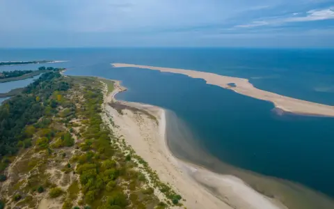 Piaszczysta wyspa na Bałtyku, otoczona wodą i zielenią, tworzy malowniczy krajobraz.