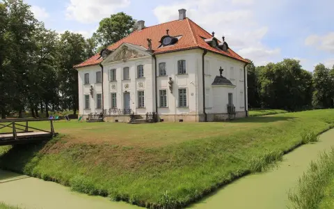 Pałac w Choroszczy otoczony fosą i zielenią, z drewnianym mostkiem prowadzącym do wejścia.