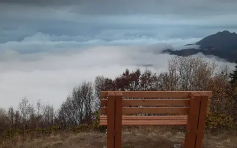 Drewniana ławka na tle morza chmur i gór. Widok z **Abchazji** zapiera dech w piersiach, idealne miejsce na chwilę zadumy.
