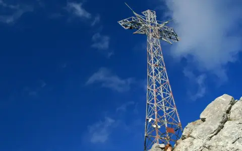 Metalowy krzyż na skalistym szczycie Giewontu pod błękitnym niebem z chmurami.