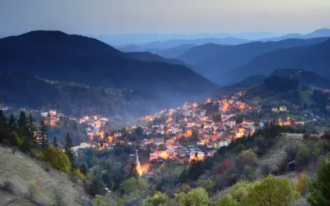 Wieczorna panorama gór w Bułgarii. W dolinie rozświetlona wioska, otoczona lasami i łagodnymi wzgórzami.