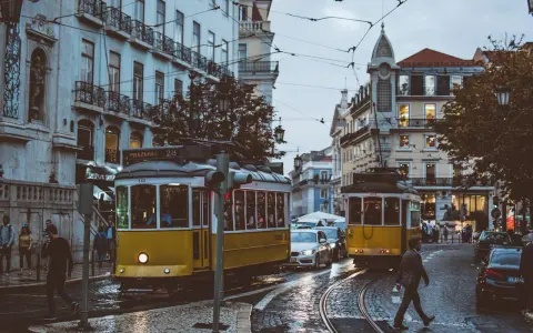 Lisbona, Portugalia. Żółte tramwaje na brukowanej ulicy, ludzie i samochody. Ceny w Portugalii mogą być różne, ale widok wart jest każdej ceny.