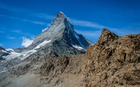 Majestatyczne szwajcaria góry z ośnieżonym szczytem Matterhorn w tle i skalistym zboczem na pierwszym planie.