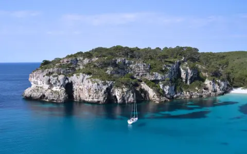 Żaglówka kołysze się na turkusowych wodach u wybrzeży skalistej zatoczki. To krajobraz z największej wyspy balearów, gdzie przyroda zachwyca.