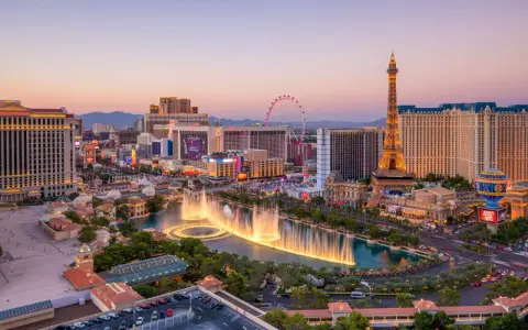 Las Vegas, miasto hazardu w USA, nocą. Widać fontanny, wieżę Eiffla i diabelski młyn.