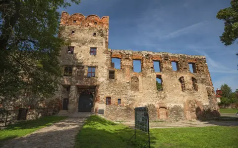 Zamek w Ząbkowicach Śląskich, ruiny z ceglaną wieżą i bramą, otoczone zielenią i błękitnym niebem.