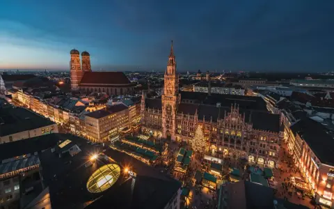 Nocny jarmark bożonarodzeniowy w Monachium. Rynek z oświetlonymi straganami i choinką, w tle Frauenkirche i Nowy Ratusz.