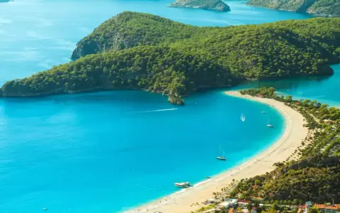 Idealne miejsce, gdzie jechać w niedzielę: turkusowa zatoka, piaszczysta plaża, zielone wzgórza i żaglówki.