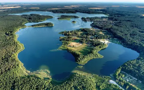 Malownicze jezioro Niesłysz otoczone lasami, z wyspami i zabudowaniami na brzegu.