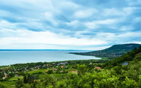 Widok na Balaton z góry, z zielonymi wzgórzami i domkami. W oddali widać jezioro i plażę.