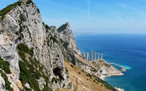 Gibraltar, brytyjskie terytorium na półwyspie iberyjskim, z górującą skałą, jaskinią i nowoczesnymi budynkami nad błękitnym morzem.