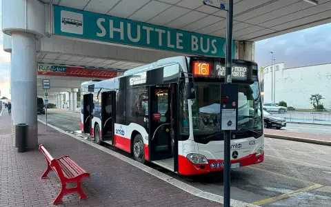 Autobus wahadłowy na przystanku lotnisko. Czerwona ławka czeka na pasażerów.