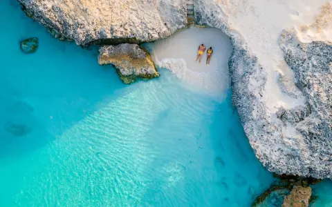 Para relaksuje się na ukrytej plaży na wyspie Aruba, otoczonej turkusową wodą i skalistymi klifami.