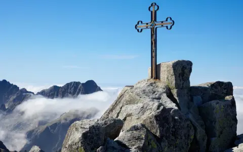 Krzyż na skalistym szczycie, najwyższy szczyt Karpat, góruje nad morzem chmur.