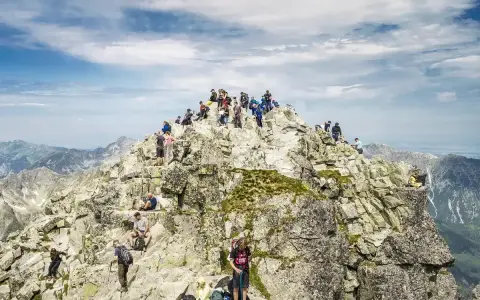 Tłum turystów na szczycie Rysów od strony polskiej. Wspinacze odpoczywają na skalistym grzbiecie, podziwiając panoramę Tatr.
