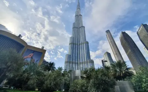Burj Khalifa, najwyższy budynek w Dubaju, wznosi się dumnie na tle błękitnego nieba z chmurami. Otoczony zielenią i innymi drapaczami chmur.