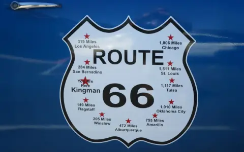 Tablica z napisem "ROUTE 66" i odległościami do miast, np. Chicago, Los Angeles, St. Louis.
