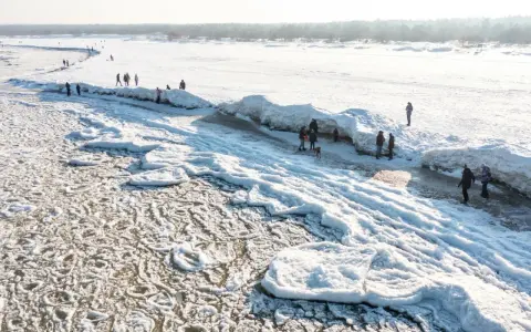Ludzie spacerują po zamarzniętej plaży z lodowymi formacjami przypominającymi góry.