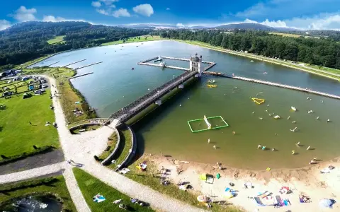 Letnia rekreacja nad zalewem, gdzie czarna góra stanowi malownicze tło dla wodnych atrakcji i wypoczynku na plaży.